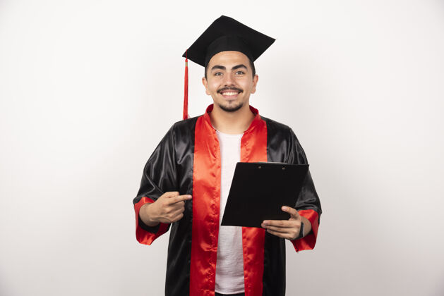 持有年轻的研究生指着白色的毕业证书长袍立场成功