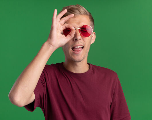 快乐快乐的年轻帅哥穿着红衬衫 戴着眼镜 在绿色的墙上显示出孤立的表情眼镜秀年轻