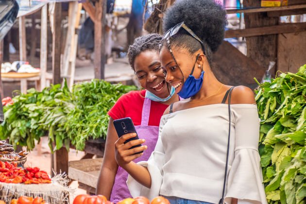 互联网两个女人在当地的非洲市场上看手机上的内容年轻人商业通讯