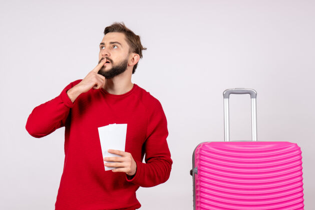 航班正面图年轻男子带着粉色包 手持白墙上的机票出行彩色度假航班出行暑期游客游客漂亮颜色