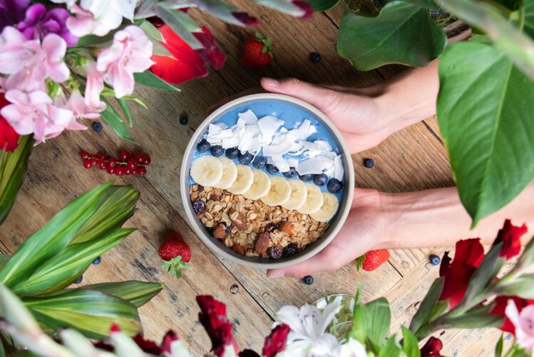 饮食顶视图是一个人拿着一个健康的蓝莓冰沙碗 里面有水果和格兰诺拉麦片新鲜谷类成熟