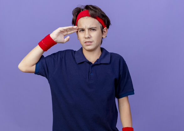 衣服年轻帅气的运动男孩戴着头带和护腕 戴着牙套 抚摸着头 看着前面的紫色墙壁上孤立的复制空间感情立场背带