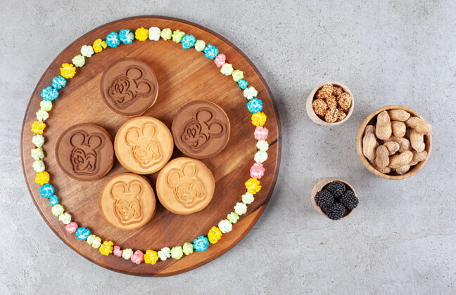 填充饼干和一圈糖果放在木板上 旁边是大理石背景上的花生和桑葚碗高质量的照片水果糕点烘焙食品