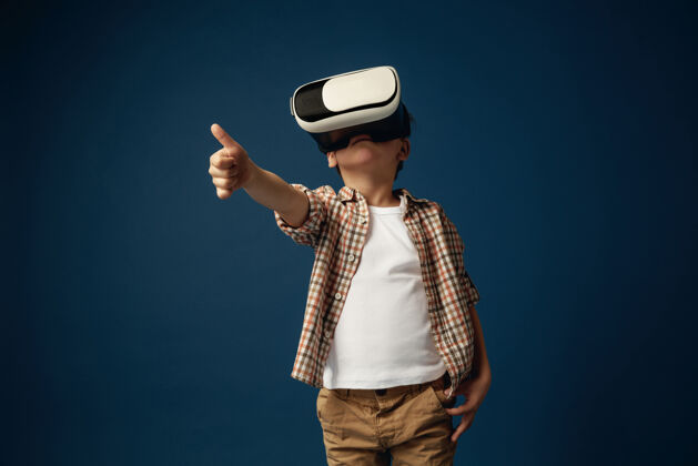 数码另一种世界观穿着牛仔裤和衬衫 戴着虚拟现实耳机眼镜的小男孩或儿童 蓝色工作室背景尖端技术的概念 视频游戏 创新未来护目镜创新