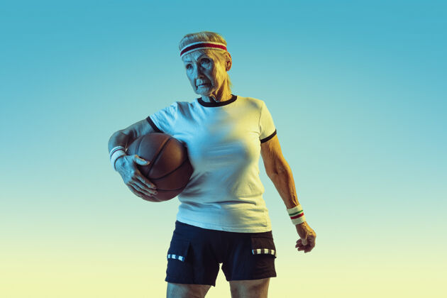 乐趣运动装的高级女性在渐变背景下打篮球 霓虹灯身材匀称的女性模特保持活跃运动 活动 运动 健康 自信的概念复制空间玩球设备