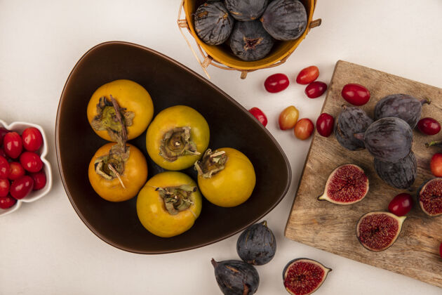 木顶视图橙色柿子水果在一个碗上与黑色无花果在一个木制的厨房板与茱萸樱桃隔离在一个白色的背景板黑樱桃