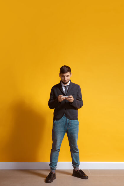 手年轻的白人男子用智能手机全身肖像隔离在黄色的墙壁白种人模型人