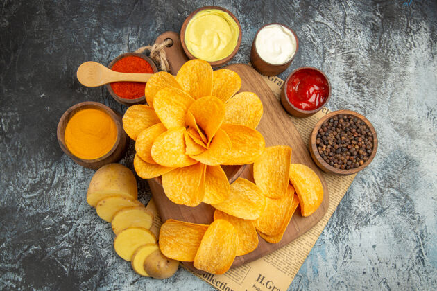 自制木制砧板上自制美味薯片的侧视图不同的香料和蛋黄酱番茄酱放在灰色桌子上的报纸上壁板食品木材