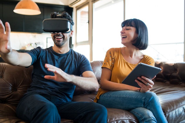 护目镜一对年轻夫妇在家里玩游戏 戴着虚拟现实眼镜玩游戏沙发享受一起