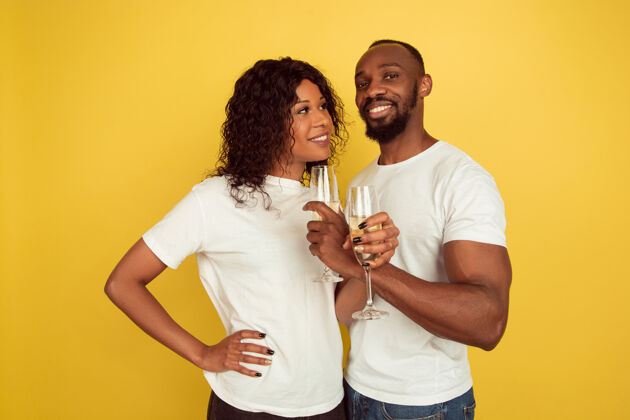心喝香槟情人节庆祝 快乐的非洲裔美国夫妇隔离在黄色工作室背景下人类情感的概念 面部表情 爱情 关系 浪漫的节日肖像民族情人节