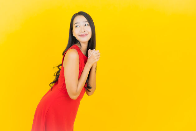 女孩肖像美丽的亚洲年轻女子穿着红色连衣裙微笑着行动在黄色的墙上人多彩年轻