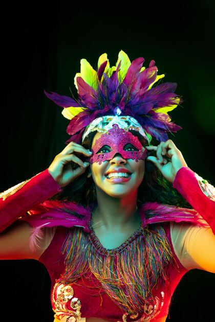 威尼斯戴着嘉年华面具和化装舞会服装的美丽年轻女子在五颜六色的灯光下神秘羽毛河