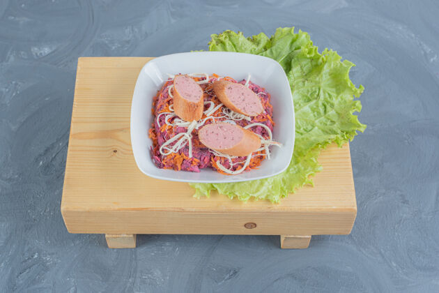 香肠一碗核桃和甜菜沙拉 放在一块木板上 上面放着莴苣叶 在大理石表面涂上香肠和奶酪可口奶酪碗