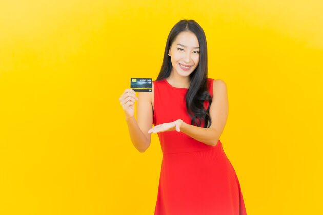 电话画像美丽的亚洲年轻女子微笑着用信用卡在黄色的墙上客户金钱肖像