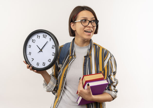 时钟快乐的年轻女学生戴着眼镜 背着书包 拿着钟 望着白纸上孤零零的一面举行欢乐壁板