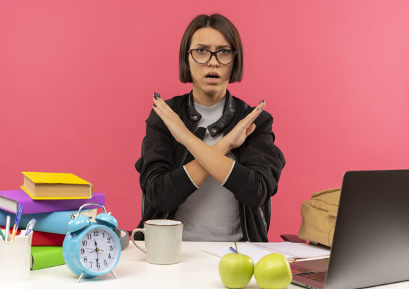作业不高兴的年轻女生戴着眼镜坐在办公桌前用大学工具做作业 手势不孤立 粉色背景姿势年轻穿着