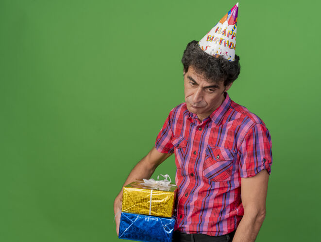 礼物悲伤的中年白种人聚会男子戴着生日帽拿着礼包看着一边孤立的绿色背景与复制空间帽子悲伤举行