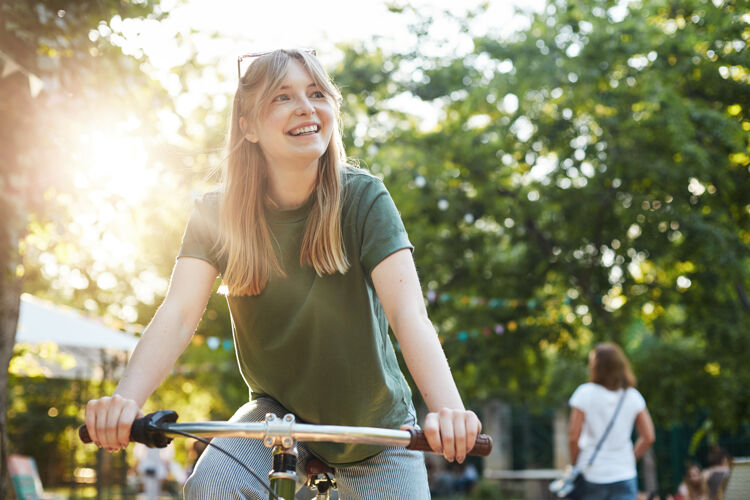 自行车在美食节期间 一位年轻漂亮的金发女郎在公园里假装骑自行车 这是一张照片绿色活跃乐趣