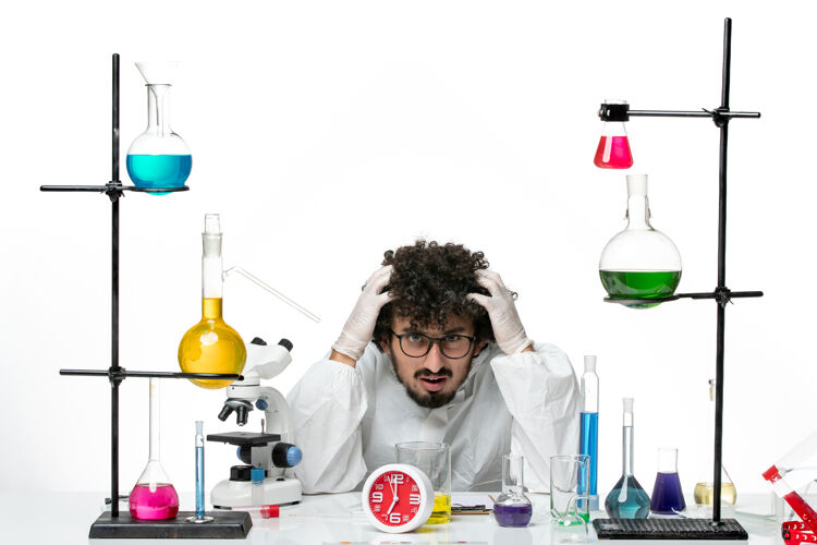 科学正面图穿着特殊套装的年轻男科学家坐在白墙上 拿着解决方案玻璃实验室罐子