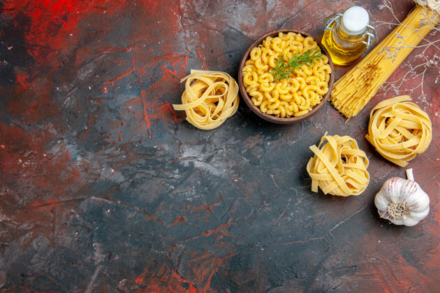 大蒜上图：在一个棕色的碗里放着三份未煮好的意大利面和蝴蝶面 在混色的桌子上放着一个葱柠檬蒜油瓶蔬菜生的食物