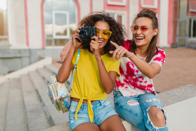 女孩快乐的年轻女孩朋友们笑眯眯地坐在街上用相机拍照 女人们一起玩得开心女性酷非洲裔