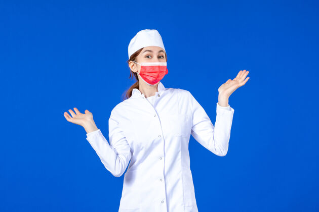 大流行正面图身着医疗服的年轻护士 蓝色墙上戴着红色防护面具成人正面红色
