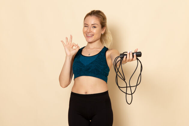 绳子正面图身着运动装的年轻女性手持跳绳在白墙上健身美容锻炼身体运动健身紧身衣服装