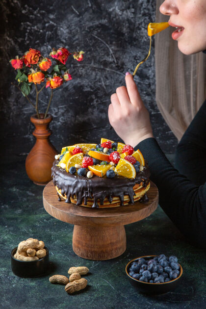 蜡烛正面图美味的巧克力蛋糕和新鲜水果得到吃的女性在黑暗的墙壁黑庆典派