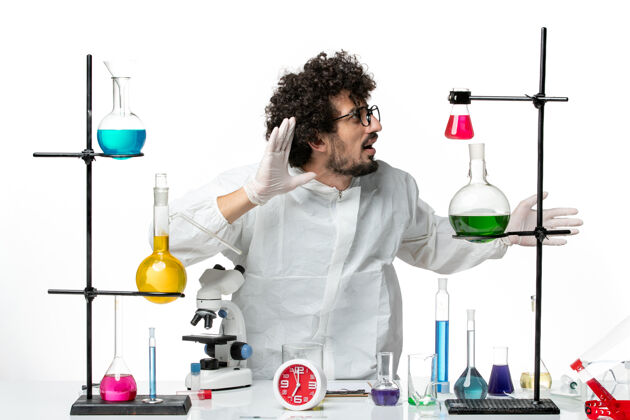 特殊正面图身穿特殊套装的年轻男性科学家站在桌子周围 白色的墙上有解决方案实验室罐子烧杯