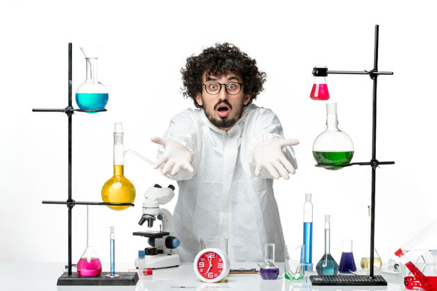 溶液正面图身着特殊套装的年轻男性科学家站在桌子周围 白色墙壁上有解决方案支架套装实验室