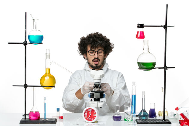 视图前视图年轻的男科学家穿着白色的特殊套装使用显微镜科学瓶子特殊