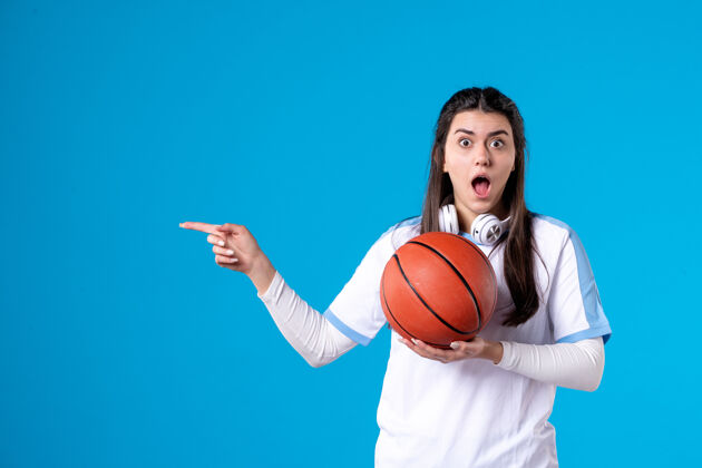 篮球正面图：蓝色墙上挂着篮球的年轻女子前面人成人
