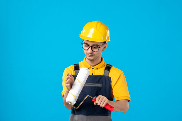 建设者前视图的男性建筑工人在制服与油漆辊在他手中的蓝色墙上油漆服务修理工
