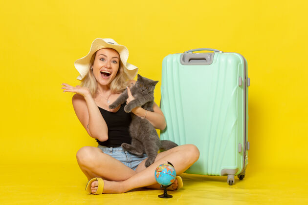 年轻正面图年轻的女性坐在她的绿色袋子抱着小猫在黄墙上旅行度假海上旅行太阳漂亮风景猫