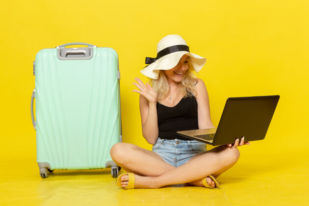 笔记本电脑前视图年轻女性使用她的笔记本电脑在黄色的墙上航行度假女性旅行太阳成人视野休闲