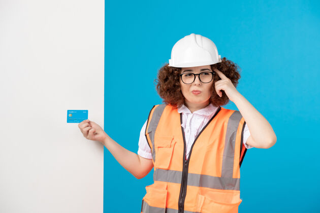 信用卡蓝色墙上穿着制服戴着头盔的女建筑工人的正视图职业人工作