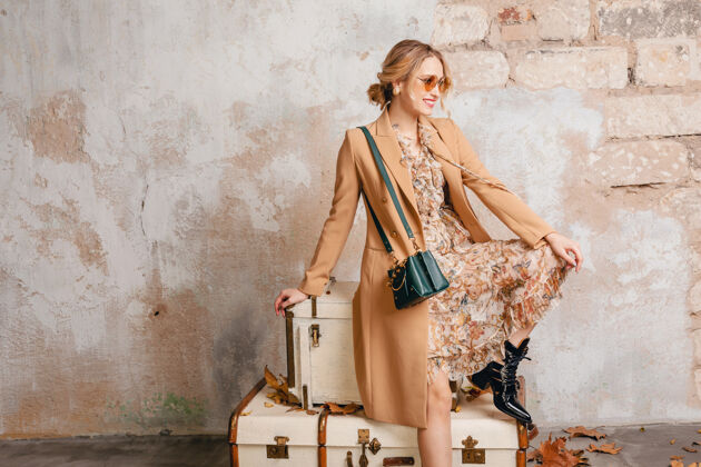 女士在街上 穿着米色外套的金发美女坐在手提箱上对着墙衣服人旅行