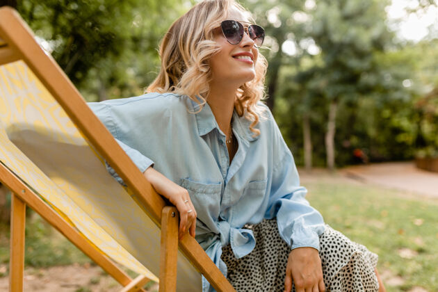 女性迷人的金发微笑的女人坐在躺椅上穿着夏天的衣服明亮春天肖像