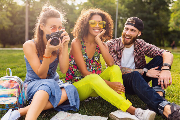 友谊快乐的年轻朋友坐在公园里谈笑风生 男女同乐 带着相机旅行时尚朋友积极