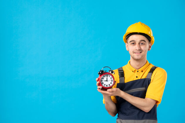 人身着制服 蓝色墙上挂着时钟的快乐男工的正面图建筑工人时间工人