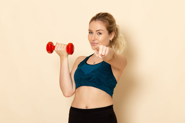 成人正面图身着运动装的年轻女性手持红色哑铃在白墙上健康运动美体锻炼器械服装身体