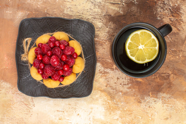 新鲜上图：棕色托盘上放着一个带有覆盆子的礼品蛋糕和一杯柠檬茶水果托盘草莓