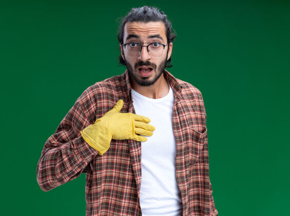 T恤年轻帅气的清洁工穿着t恤 戴着手套 把自己的手孤立在绿色的墙上惊喜年轻清洁