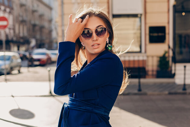 西装在阳光明媚的夏日 穿着蓝色西装戴着墨镜走在街上的性感时尚女人的肖像包魅力优雅
