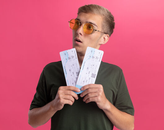 壁板惊讶地看着身边穿着绿衬衫戴着眼镜的年轻帅哥 手里拿着隔离在粉红色墙上的票票惊喜举行