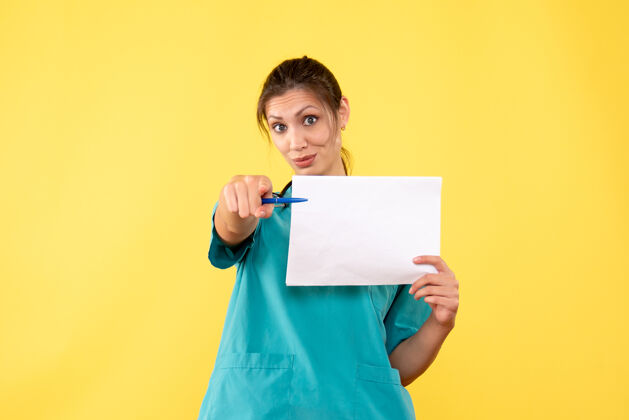 视图正面图黄色背景上穿着医疗衫的女医生拿着纸分析前面健康医学