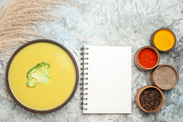 盘子在一个棕色碗里的奶油西兰花汤和笔记本旁边的不同香料的水平视图纸容器饭