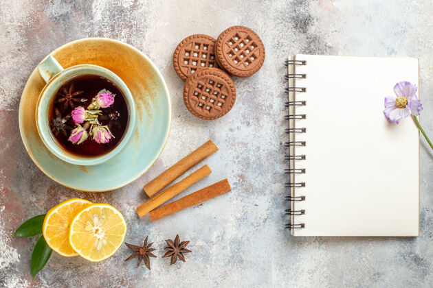切片一杯花草茶饼干和肉桂柠檬片和笔记本放在白色的桌子上八角饼干凉茶