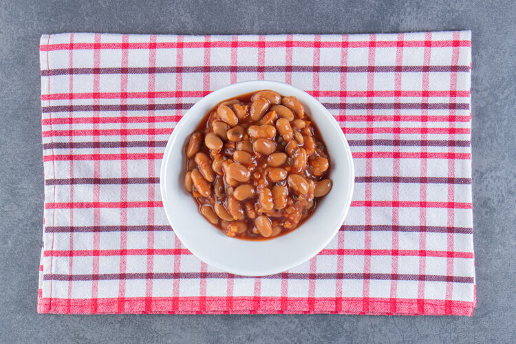豆子美味的一碗烤豆子放在茶巾上 放在蓝色的表面上好吃的自制的好吃的