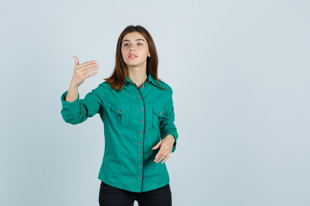 女孩年轻女孩伸出手 手里拿着一件想象中的东西 穿着绿色上衣 黑色裤子 神情专注 俯视前方课堂课电脑课衬衫